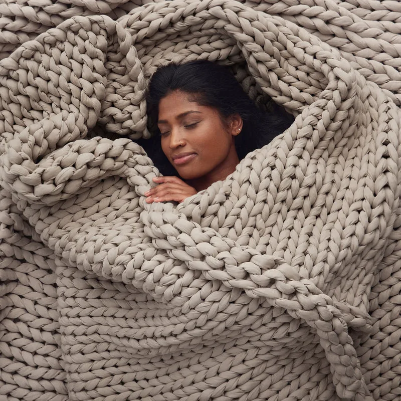 A person wrapped in a chunky Bearaby Tree Napper weighted blanket