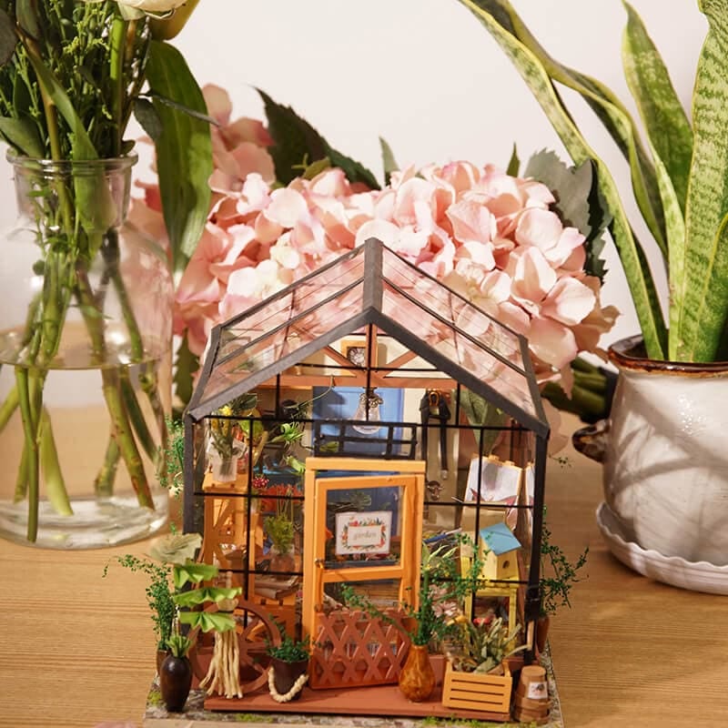 Completed Rolife Cathy’s Flower House miniature greenhouse displayed among real flowers and plants