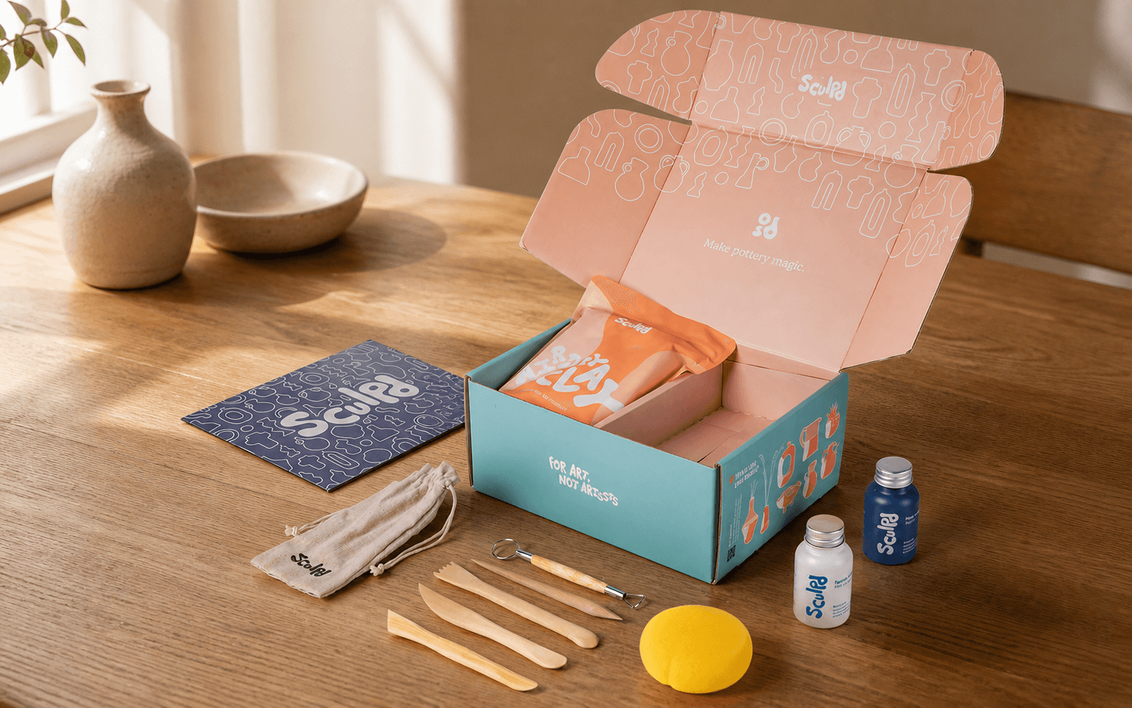 Representative product-led scene of the Sculpd pottery kit with clay, tools, sponge, and finishing bottles
